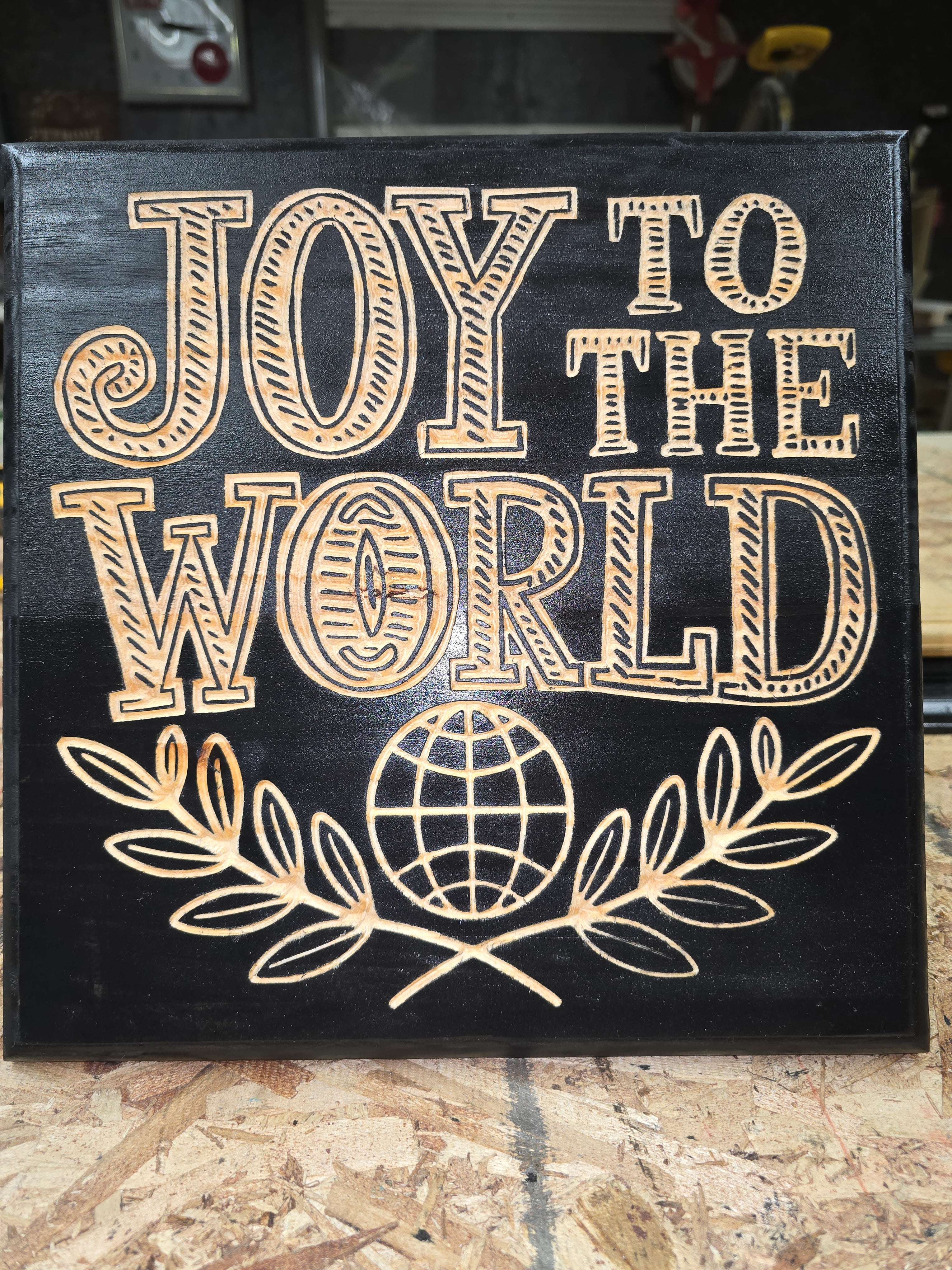 Decorative plaque with 'Joy to the World' text and a globe design on a wooden surface