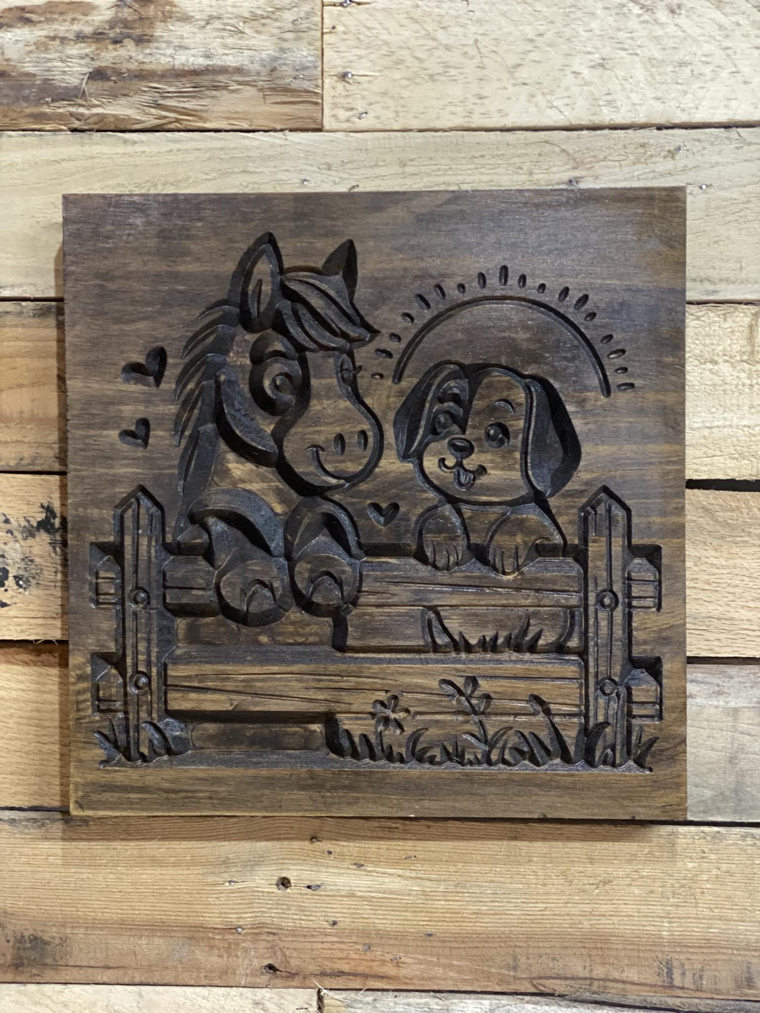 Wooden plaque with engraved design of a horse and dog behind a fence on a wooden background