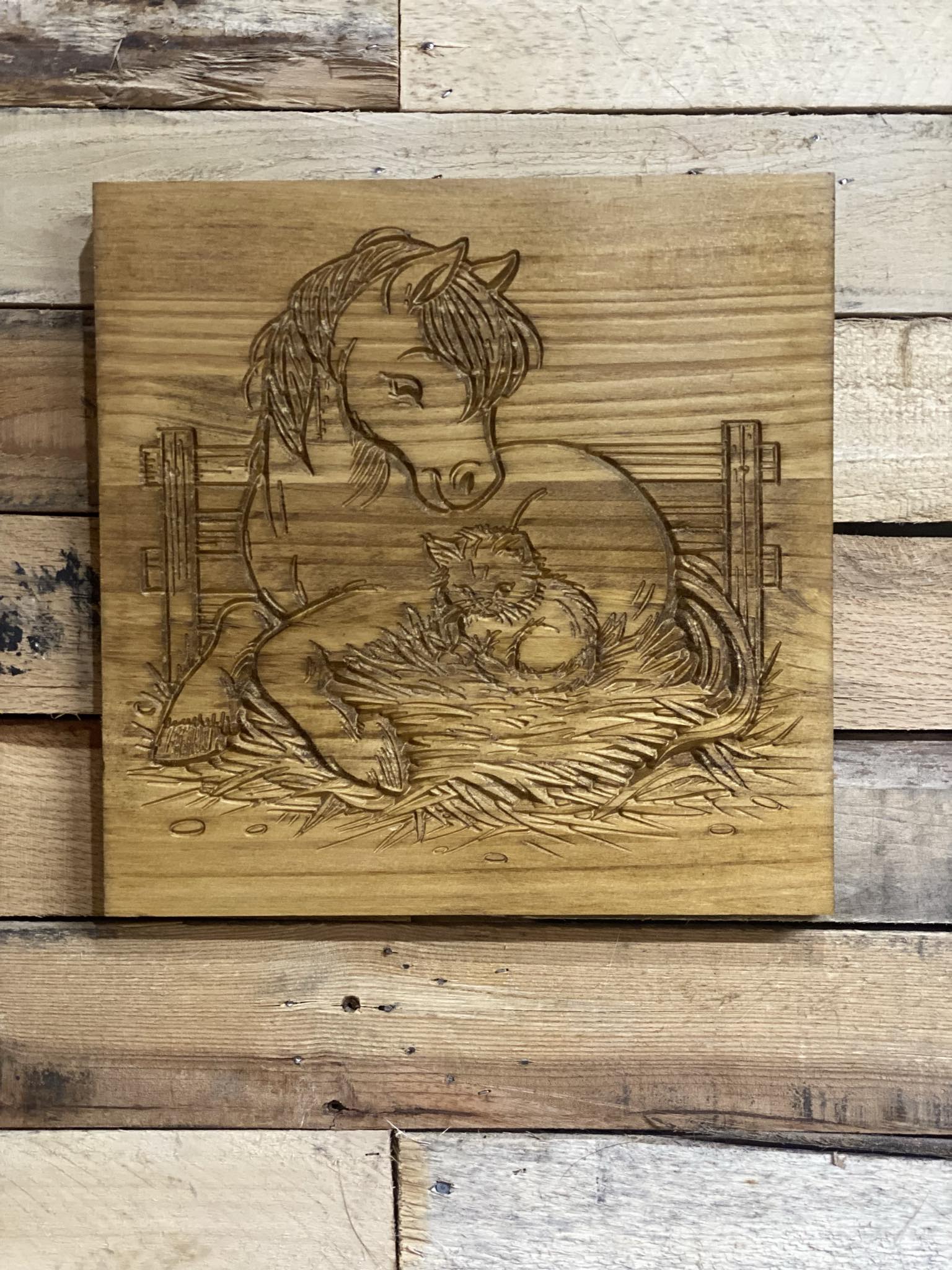 Wooden plaque with engraved design of a horse and a cat on a wooden background